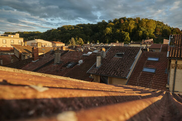 Scenic Rooftop View of a Historic European Town at Sunset with a Church, Antennas, and Chimneys Illuminated by Golden Hour Light, Capturing the Tranquil Atmosphere of Old Architecture 