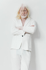 Stylish elderly man in a white suit standing confidently against a light background The man s long white hair and beard, alongside his attire, convey elegance and modern fashion