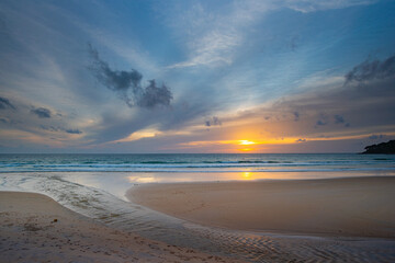 Obraz premium A stunning sunset over the ocean with soft golden light reflecting on the water, featuring silhouettes of people walking along the shore.Water flows from a small stream into the sea..