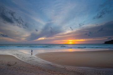 A serene beach scene at dusk, showcasing a vivid sunset with colorful clouds reflected on the calm waters and wet sand. amazing sky in sunset over Karon beach Phuket. sweet sky background