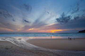 A serene beach scene at dusk, showcasing a vivid sunset with colorful clouds reflected on the calm waters and wet sand. amazing sky in sunset over Karon beach Phuket. sweet sky background