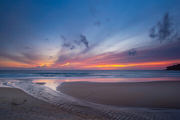 A serene beach scene at dusk, showcasing a vivid sunset with colorful clouds reflected on the calm waters and wet sand. amazing sky in sunset over Karon beach Phuket. sweet sky background