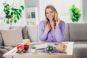 Photo of attractive young woman sit couch talk phone table write notebook dressed purple outfit cozy day light home interior living room