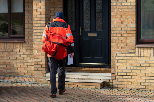 Postman or Mailman in UK posting mail through the letter or mailbox of a house front door