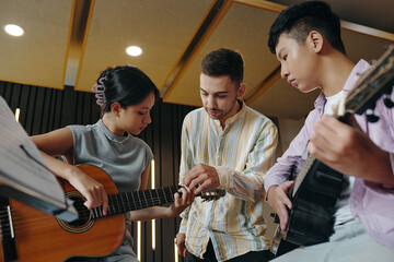 Music instructor teaching guitar techniques to two young students. The students are holding guitars...
