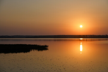 Obraz premium the beauty of a sunset over a calm lake, with the sun's reflection shimmering across the water