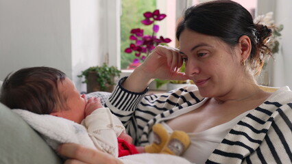 Mother reclining on a sofa, smiling softly as she gazes at her newborn baby in her arms, surrounded...