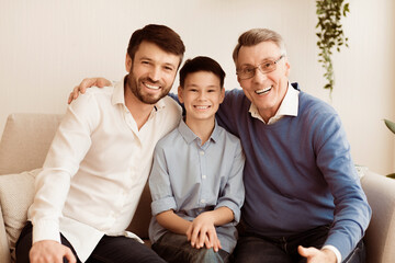 Male Generation. Happy Grandfather With Son And Grandson Smiling At Camera Hugging Sitting Together On Couch At Home.