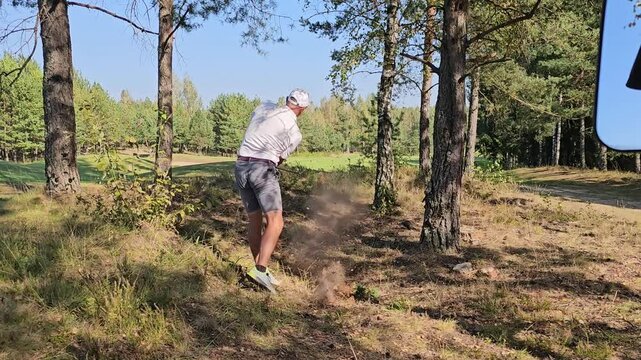 Golfer takes a tricky shot from the rough in a scenic forested area on a sunny day