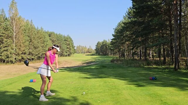 A golfer prepares for a swing on a serene course surrounded by tall trees in sunny weather