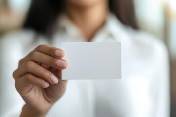 Close-up photo of a woman's hand holding a blank business card, wearing a white shirt, against a modern office background with a bokeh effect Generative AI