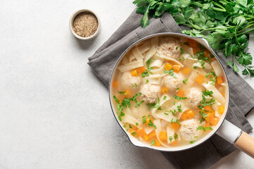 Chicken soup with meatballs and noodles in light saucepan on white background with copy space