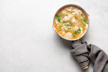 Chicken soup with meatballs and noodles in light saucepan on white background with copy space