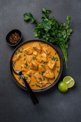 Chicken curry in black bowl with green herbs and lime on  dark background with copy space. Traditional asian food