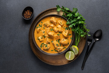 Chicken curry in black bowl with green herbs and lime on copper tray and dark background with copy space. Traditional asian food