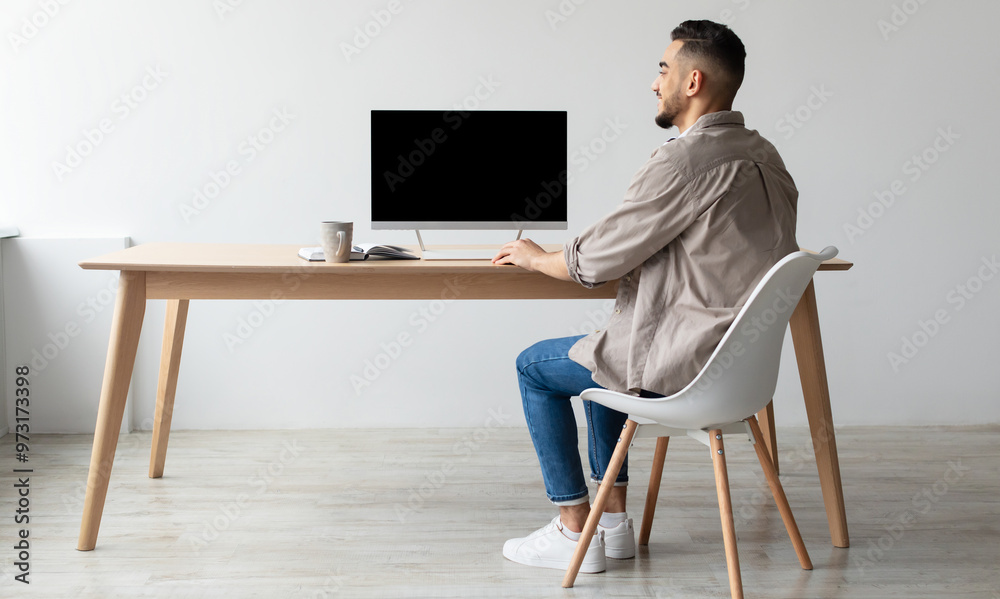 Aufkleber Rear Back View Of Happy Smiling Arab Man Looking At Pc Computer With Blank Black Screen For Mock Up Template Sitting At Desk At Home Office, Free Copy Space. People, Technology, Remote Work Concept