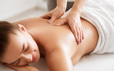 Young girl receiving back massage with closed eyes in spa center, closeup