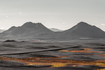 Icelandic black rock highlands with mountains in the background, a road leading to the horizon, a...