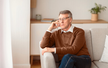 Fototapeta premium Depression In Older Age. Sad Senior Man Thinking About Retirement Sitting On Couch At Home. Selective Focus, Copy Space