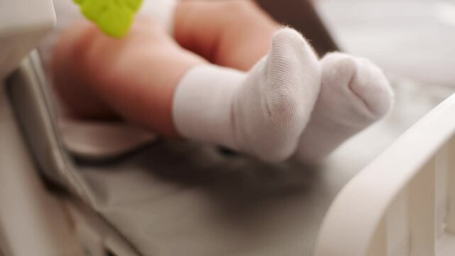 Close-up of newborn baby feet in white socks, awake in baby chair, leading active lifestyle, soft focus. Concept of children health, baby wakefulness, child development. Children's day.
