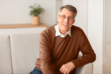 Happiness In Old Age. Positive Elderly Gentleman Smiling Looking At Camera Sitting On Sofa At Home.