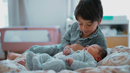 Older brother lying next to newborn sibling on a bed, gazing lovingly at the baby, highlighting the...
