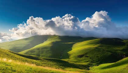 Obraz premium Sunlit Green Hills with Rolling Clouds Overhead on a Clear Blue Sky Day, Capturing the Serene Beauty of a Misty Mountain Landscape with Vivid Grass and Dramatic Light Play in the Early Morning
