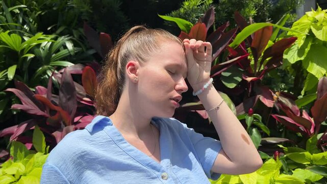 Young woman feeling bad, suffering from sunstroke in tropical park at summer