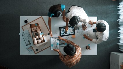Top down view of architect engineer team discussing and point at tablet display construction at table with blueprint and house model at meeting. Diverse designer planning design house. Alimentation.