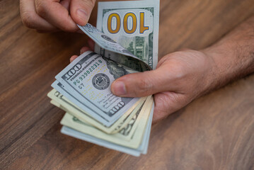 Hands counting US dollar banknotes on a wooden surface. Cash handling and financial management...