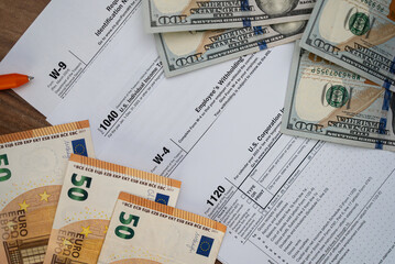 Tax forms and currency on a wooden desk, featuring U.S. dollars and euros. Financial paperwork for tax filing season. Concept of tax preparation, accounting, and financial management 