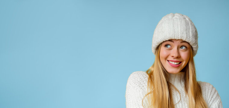 Ooops. Cute blonde girl in white winter hat looking at copy space, panorama