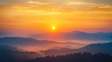 Obraz premium A breathtaking sunrise paints the sky in vibrant orange hues, illuminating misty mountain ranges with a soft, golden light. The scene evokes a sense of tranquility and serenity, capturing the beauty o