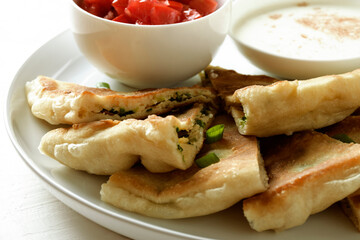 Flatbreads stuffed with green onions, cut into pieces, tomatoes, sour cream. Close-up.