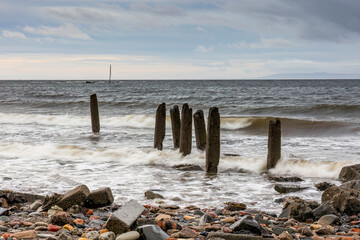 Decaying old pier wood posts Ayr Harbour beside sea MV Kaffir abandoned Clyde puffer wreck in...