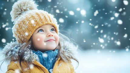 Fototapeta premium A young girl wearing a yellow hat and a blue scarf is standing in the snow