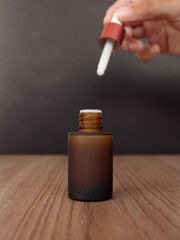 Dropper bottle in hand on dark background. Skincare product concept. Front view.