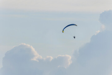 Recreational adventure sport paraglider free flying sitting in a harness and propeller motor suspended below colorful fabric wing over English countryside