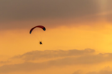 Paraglider free flying in harness with propeller motor and colorful fabric wing at sunset