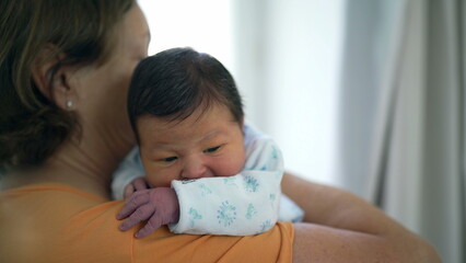 Grandmother gently holding her newborn grandchild close to her shoulder, offering security and comfort. baby’s calm demeanor highlights the nurturing care and bond between them