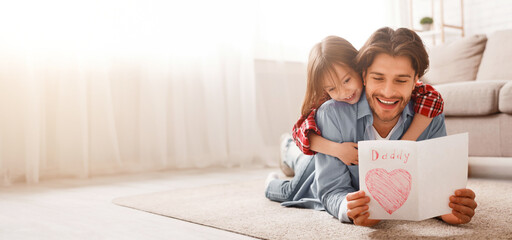 Happy father reading greeting self-made card while bonding with daughter on floor at home, free space