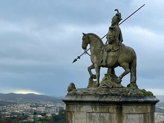 Obraz premium Stone knight statue with spear in the Sameiro Sanctuary. In the background, the city of Braga with cloudy skies. Bom Jesus do Monte, Portugal.