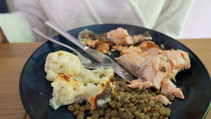 Partially eaten grilled salmon with a side of mashed potatoes and lentils on a dark plate, highlighting the textures and remaining portions of this healthy and satisfying meal