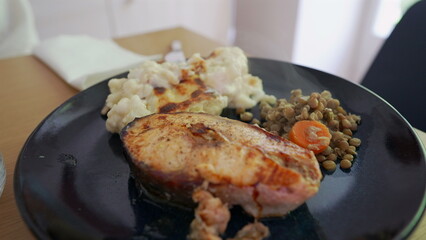 Close-up of a delicious home-cooked meal featuring grilled fish, creamy mashed potatoes, and a side of lentils with carrots. steam rising from the plate adds warmth and freshness to the dish