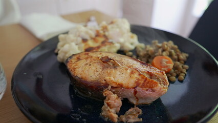 Close-up of a delicious home-cooked meal featuring grilled fish, creamy mashed potatoes, and a side of lentils with carrots. steam rising from the plate adds warmth and freshness to the dish