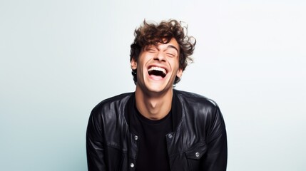 Fototapeta premium A young man in a black leather jacket laughs heartily against a minimalist light-colored background.