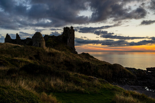 Dunure Castle and Dovecot ruins at sunset beside Firth of Clyde sea with grass and rocky shore