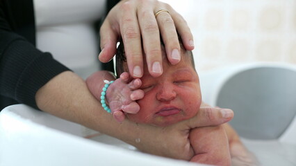 Newborn baby being lovingly cradled in a bath, with a hand gently resting on the baby's head for comfort and reassurance. baby's peaceful expression
