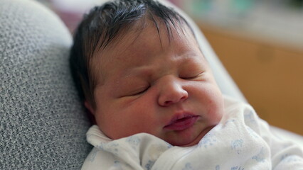 Close-up of a newborn baby with dark hair, displaying a curious and slightly furrowed brow. The baby's intense gaze suggests deep thought or early concentration