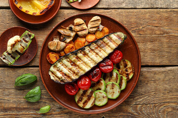 Plates with grilled vegetables and basil on wooden background